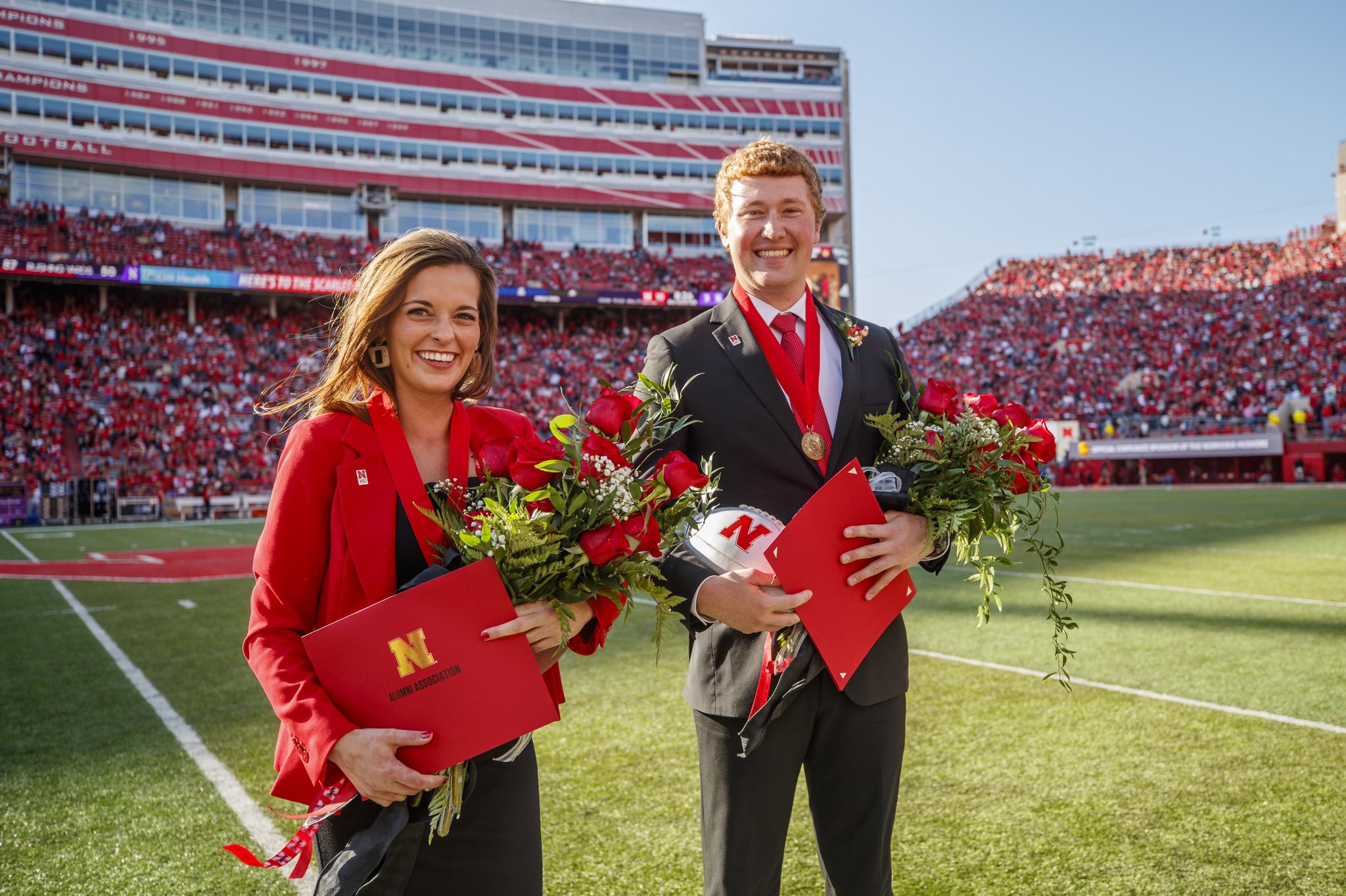 2019 Homecoming Queen and King stand with flowers and medals in the middle of the football field at halftime