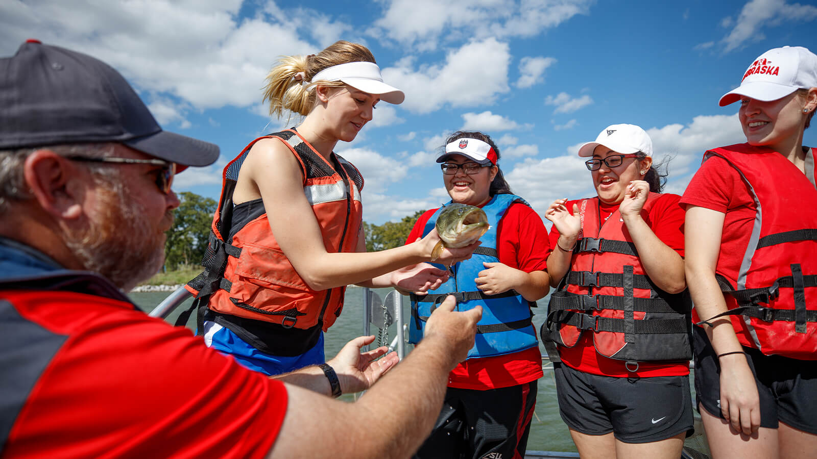 Students in lifejackets on a boat looking at a fish