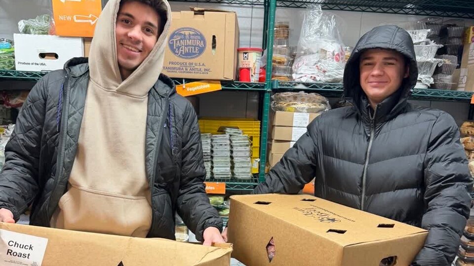 Two students hold large boxes of beef while volunteering at a food bank.