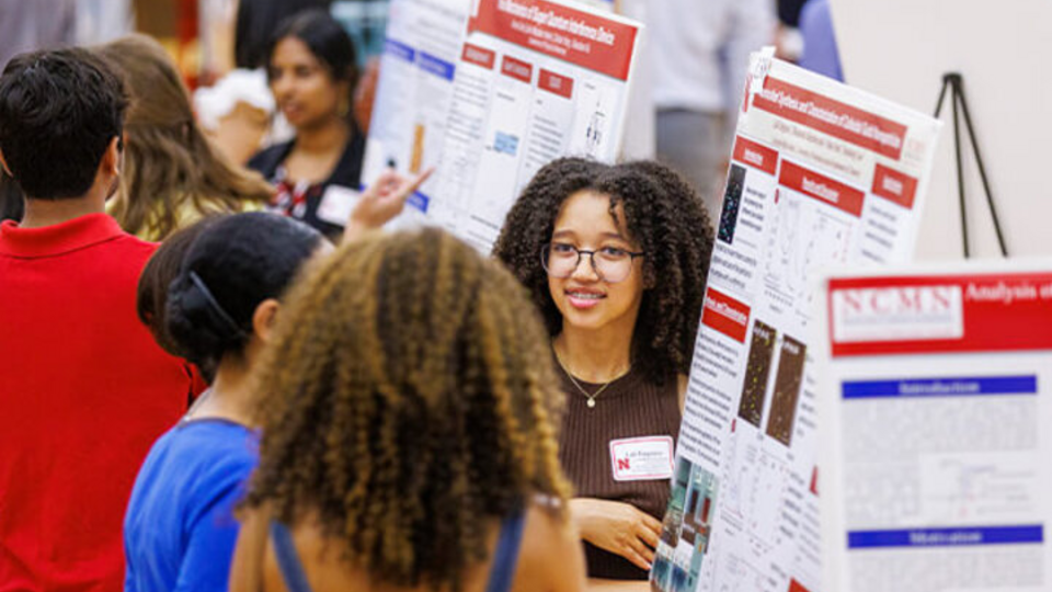 A student explains her research poster to two other students during a research poster session.