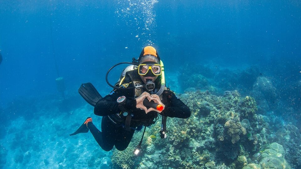 A student makes a heart shape with her hands while scuba diving in Australia