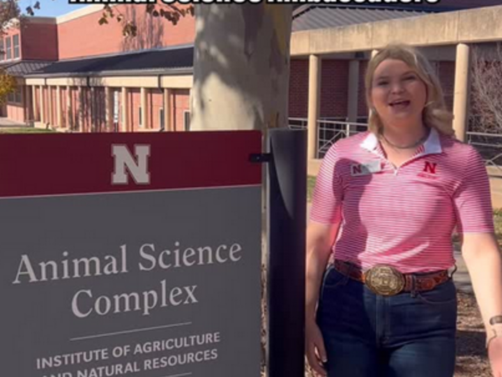 An Animal Science Ambassador stands next to the Animal Science Complex sign