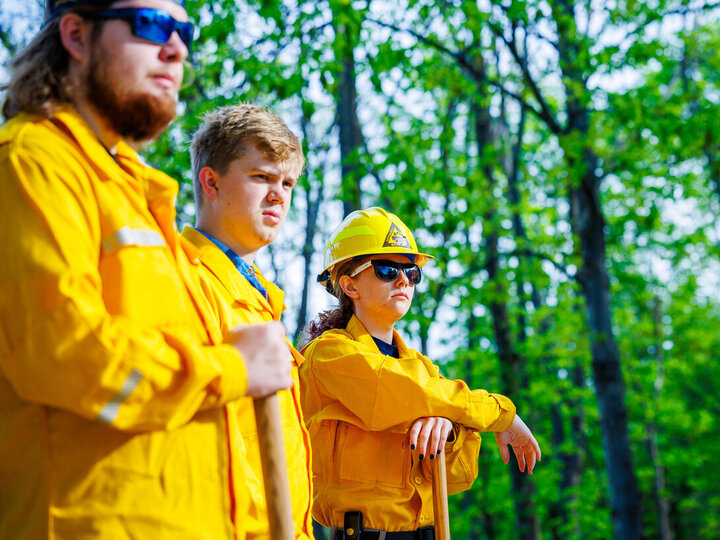 Three students dressed in fire gear stand in a wooded area as part of Red Card Training