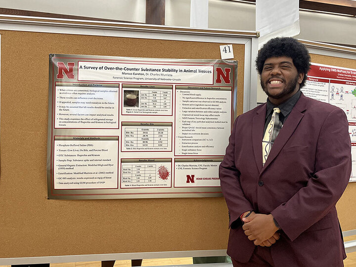 Marcus Cureton poses next to his research poster on over-the-counter substance stability in animal tissues.