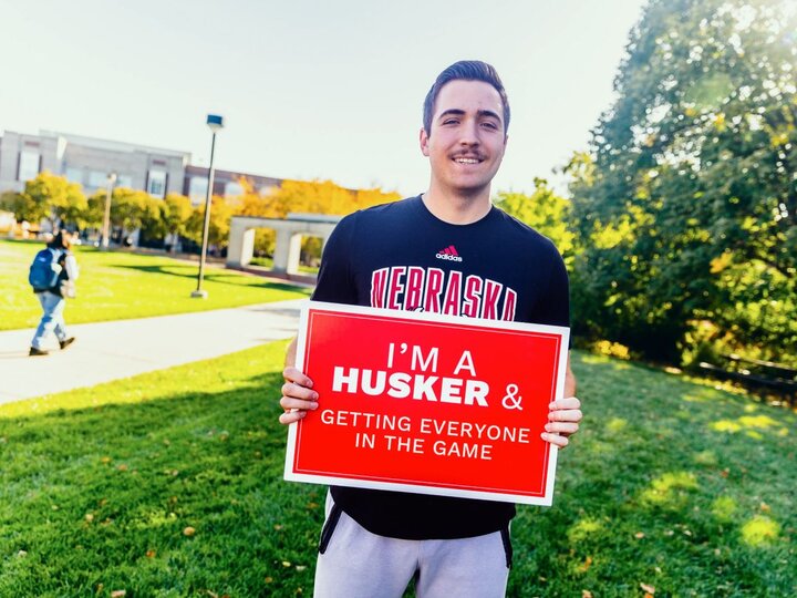 Student holding a sign that states "I'm a Husker and I'm getting everyone into the game".