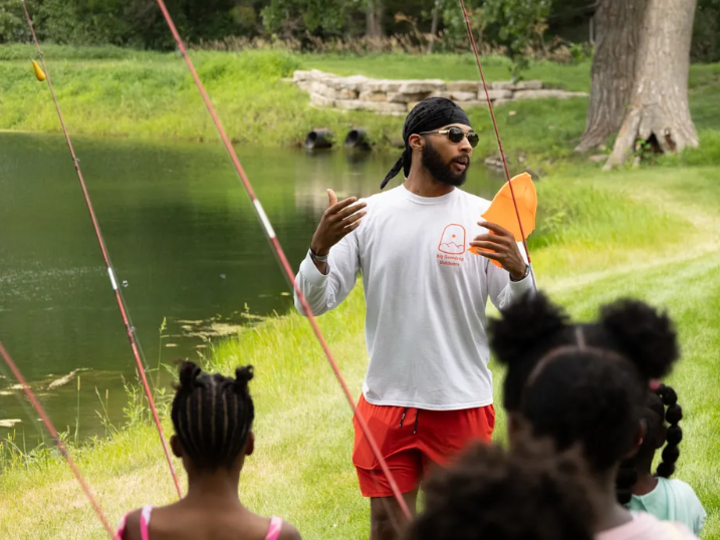 Elijah Riley gives fishing instructions to a group of kids holding fishing poles.