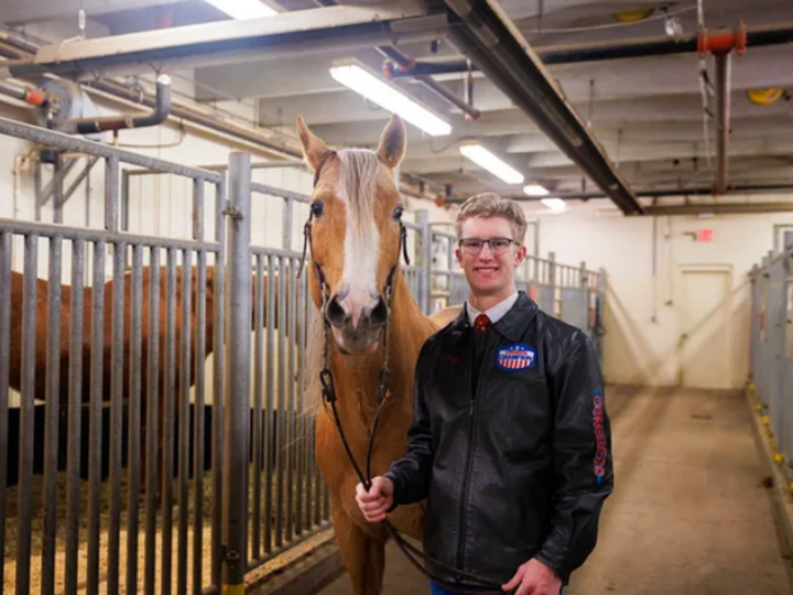 A member of the Horse Judging Team poses with a horse in the horse barn.