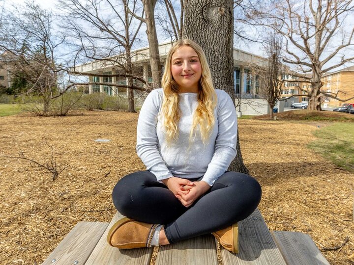 Hannah Haun sits on top of a picnic table underneath a large shade tree on East Campus.