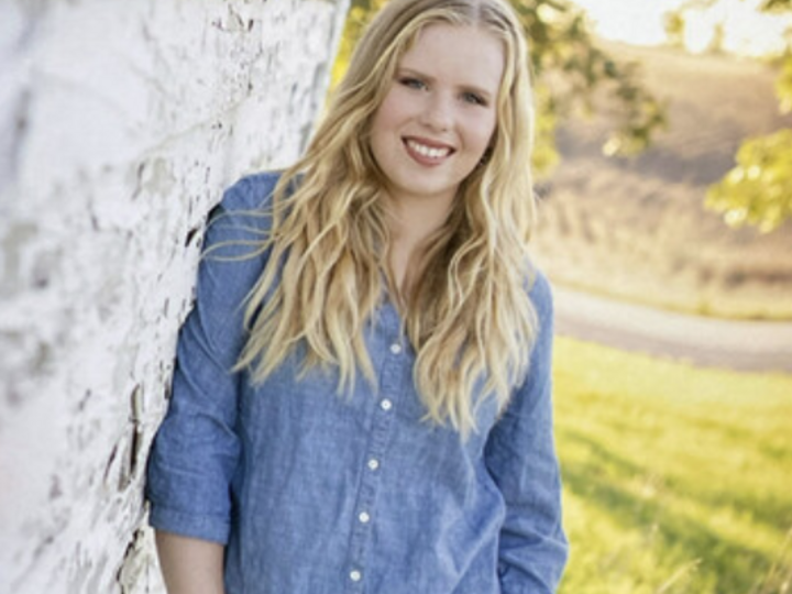 Paige McKenzie poses for a photo leaning against a stone wall.