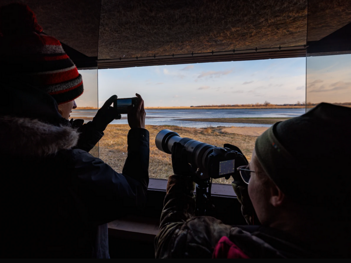 Two students take photos of the Platte River as sandhill cranes arrive to roost for the evening