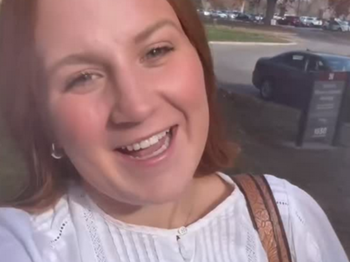A female student smiles at the camera as she walks across campus.